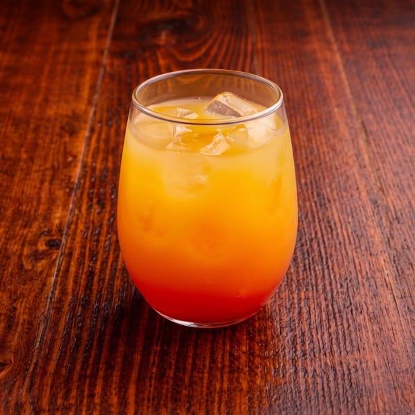 Orange and red layered drink with ice in a glass on a dark wooden table.