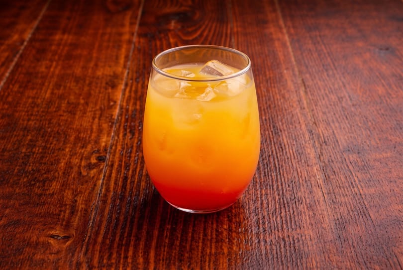 Orange and red layered drink with ice in a glass on a dark wooden table.