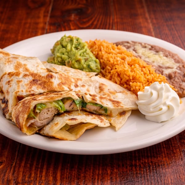 Chicken quesadillas with guacamole, Mexican rice, refried beans, and sour cream on a white plate.
